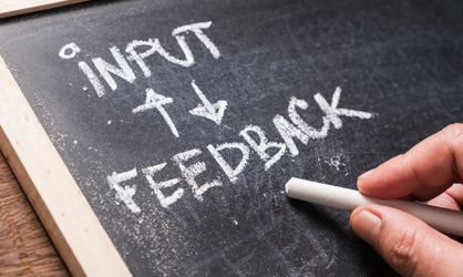 Dark chalkboard with a light wood border with the words input and feedback written in white chalk with directional arrows between the words.